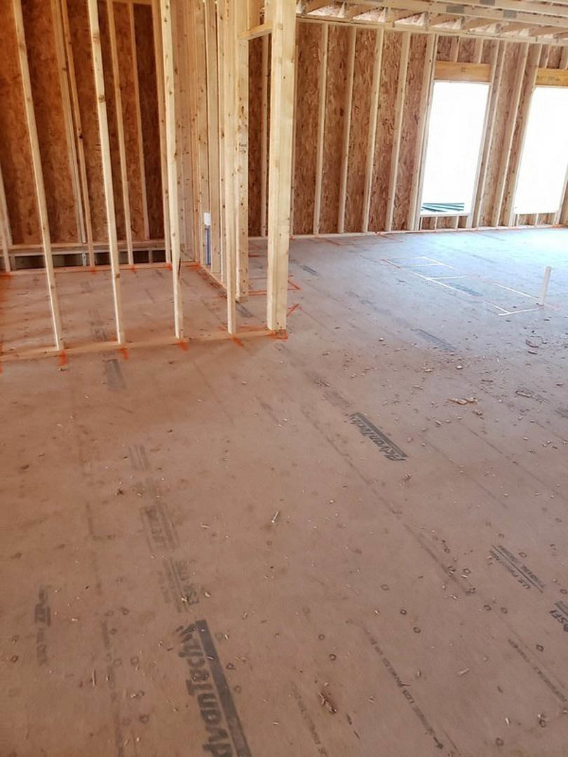 unfinished room with exposed wood framing, beams, and flooring; sunlight streaming through a window highlights beige insulation and composite materials