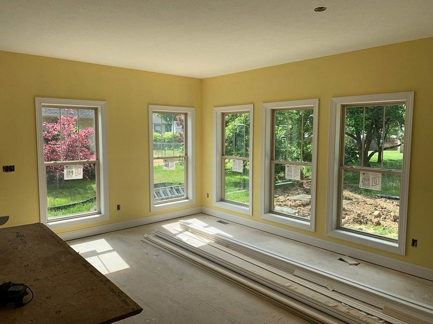Spacious room featuring multiple large windows, natural wood flooring, white walls, and a close-up of a wooden table; window sill and white metal door with black and white accents