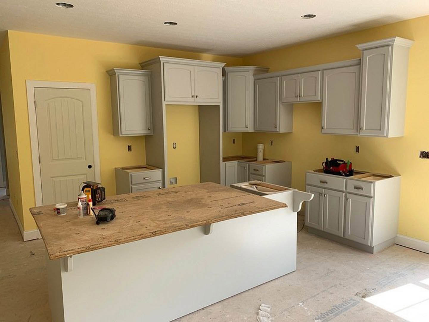 White kitchen cabinets with black handles, light stone countertop featuring a tape measure, stainless steel sink, tiled backsplash, and wood flooring