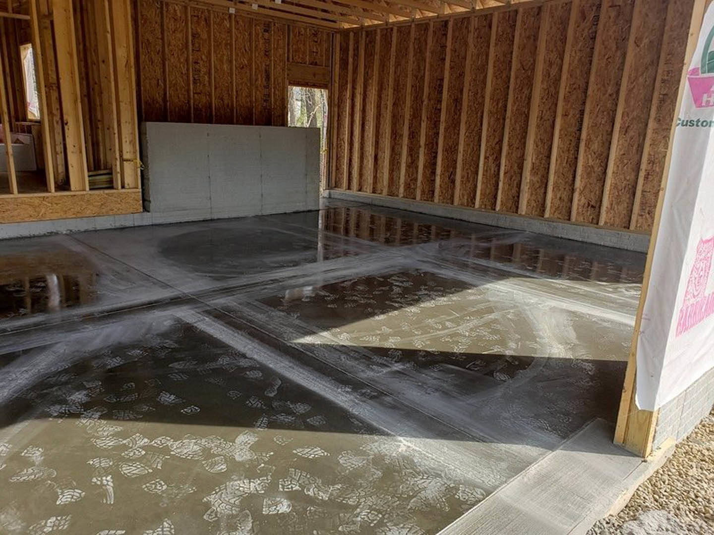 Concrete floor with visible footprints, white wall featuring pink graffiti, adjacent wooden wall with exposed beams.