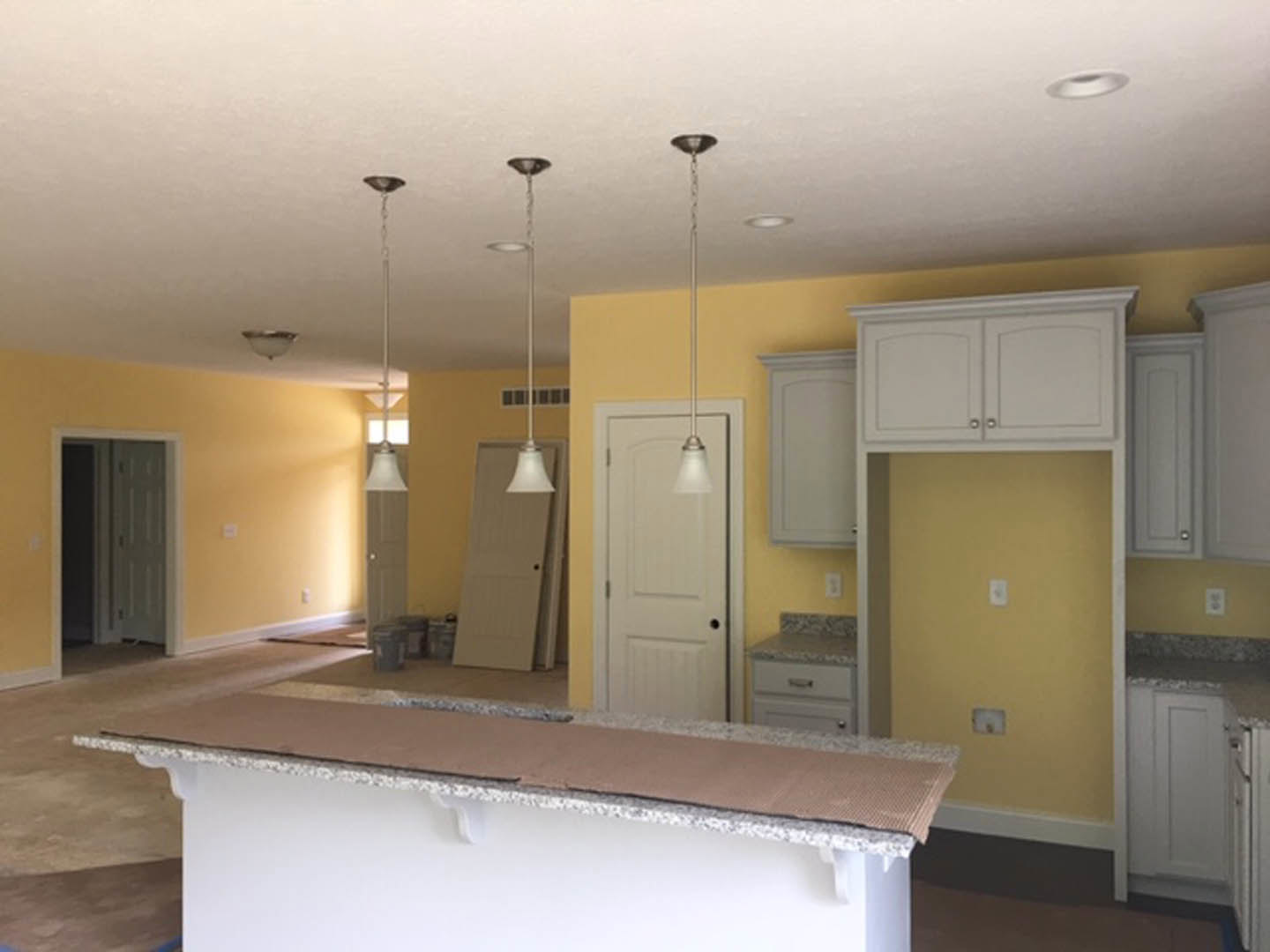 Modern kitchen featuring white cabinetry, tile backsplash, stone countertop, stainless steel sink, and light wood flooring; white door with glass panel and black hardware visible
