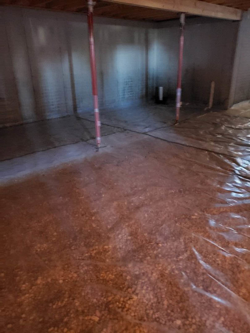 Concrete floor with plastic sheeting, red metal pole, white table with red object, unfinished walls in residential interior