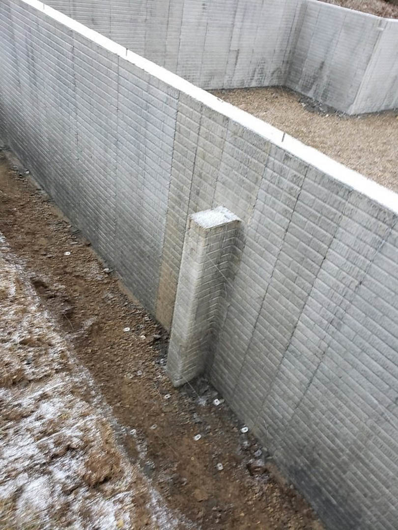 Concrete exterior wall with circular hole, surrounded by dirt and grass, showing rough cement finish and winter outdoor setting