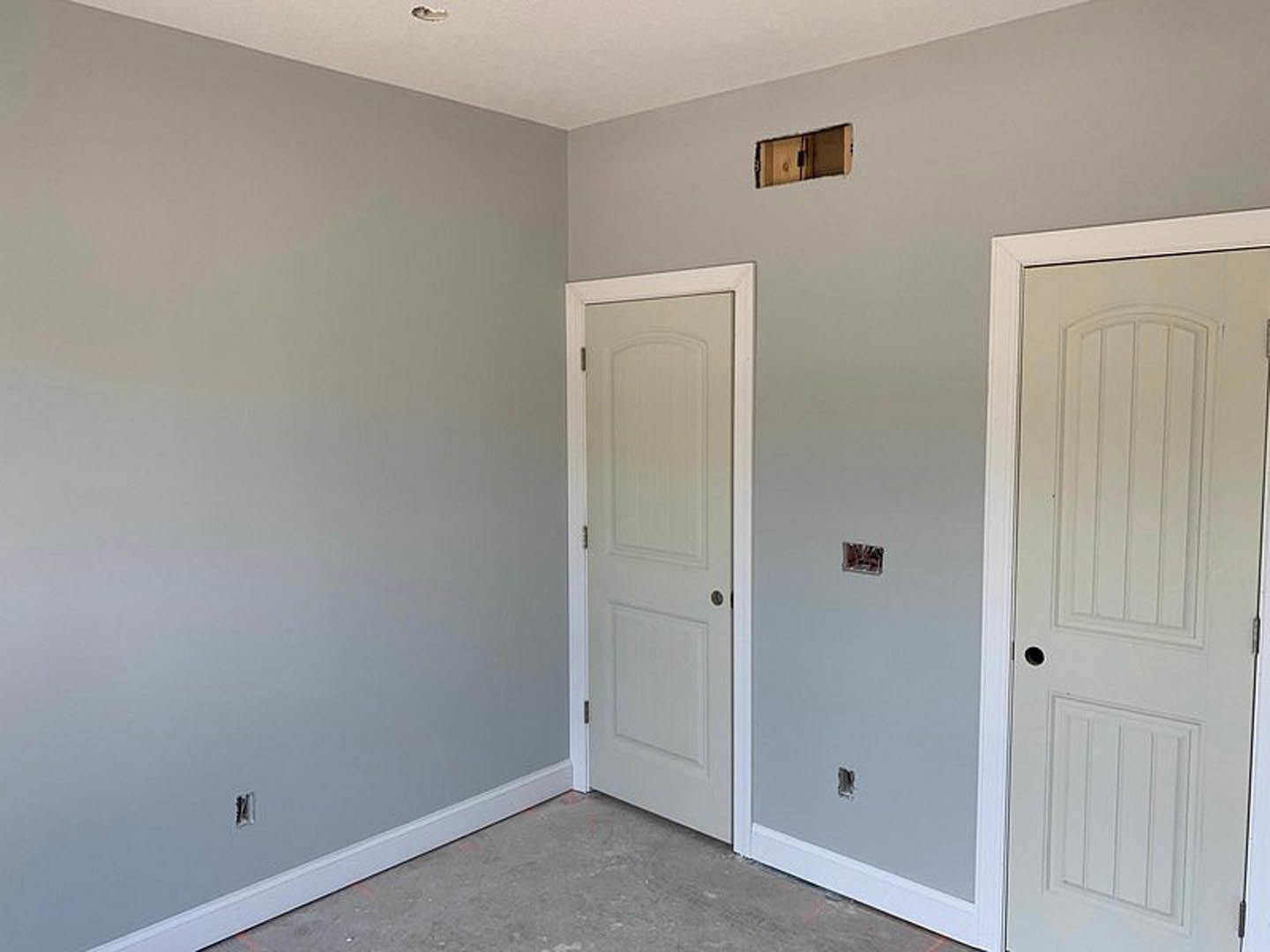 White paneled door with silver doorknob set in a plaster wall, grey laminate flooring, electrical outlet, and wooden storage box visible.