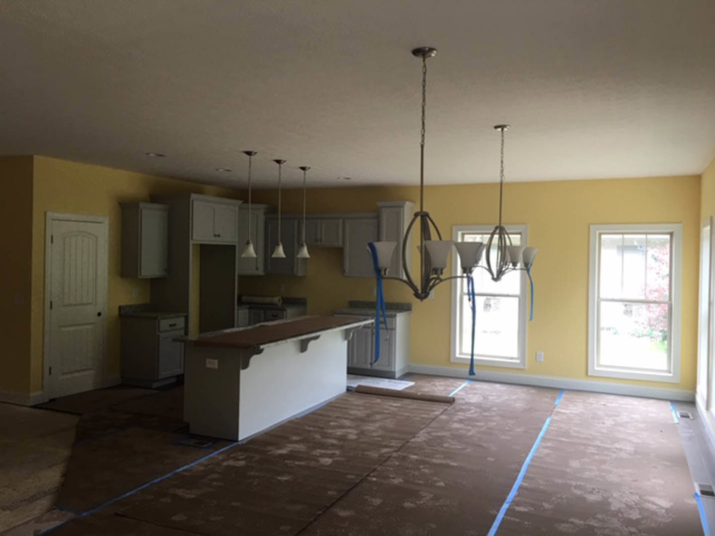 Modern kitchen featuring a white island with bar seating, tile flooring, white cabinetry, black hardware, a window above the sink, and a chandelier overhead.