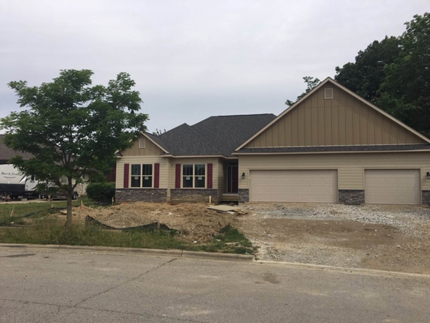 Two-story house with white brick exterior, attached garage, paved driveway, and mature tree in front yard