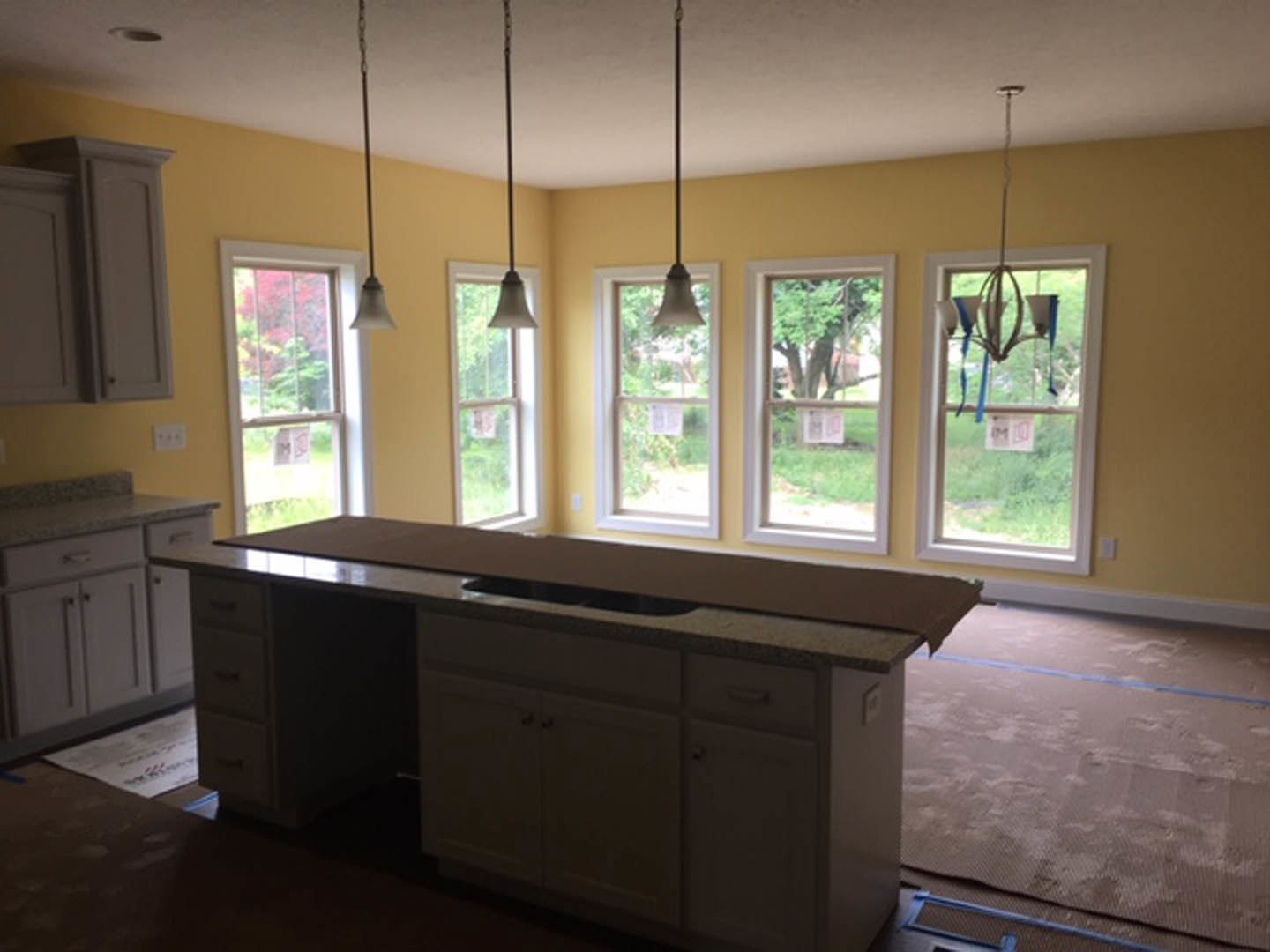 Modern kitchen with white countertops, stainless steel sink, wood cabinetry, large windows overlooking trees, and natural light illuminating the space