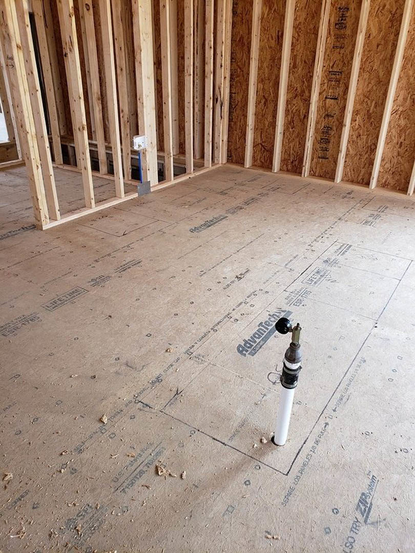 White pipe emerging from unfinished floor in a room with exposed wood beams and partially constructed walls