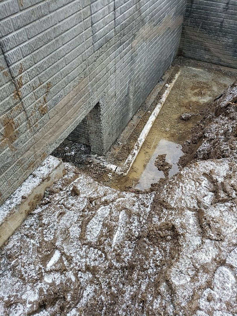 Dirty puddle of mud beside a brick exterior wall with patches of snow on concrete ground in winter