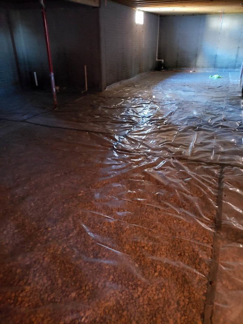 Plastic sheeting covers the floor of a room, with a red support pole and overhead light illuminating white walls and ceiling.