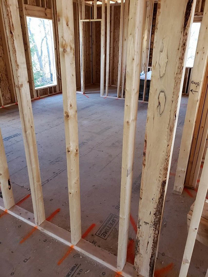 Living room with exposed wood ceiling beams, large windows overlooking trees, light-colored walls, and hardwood flooring