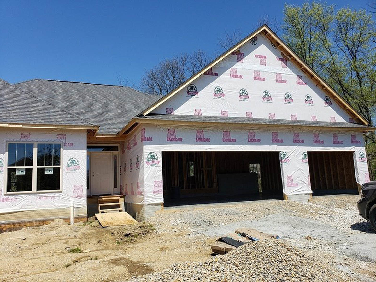 Partially built home wrapped in white weatherproof sheeting, white door with black handle, window displaying construction signs, logo printed on exterior surface, construction tire