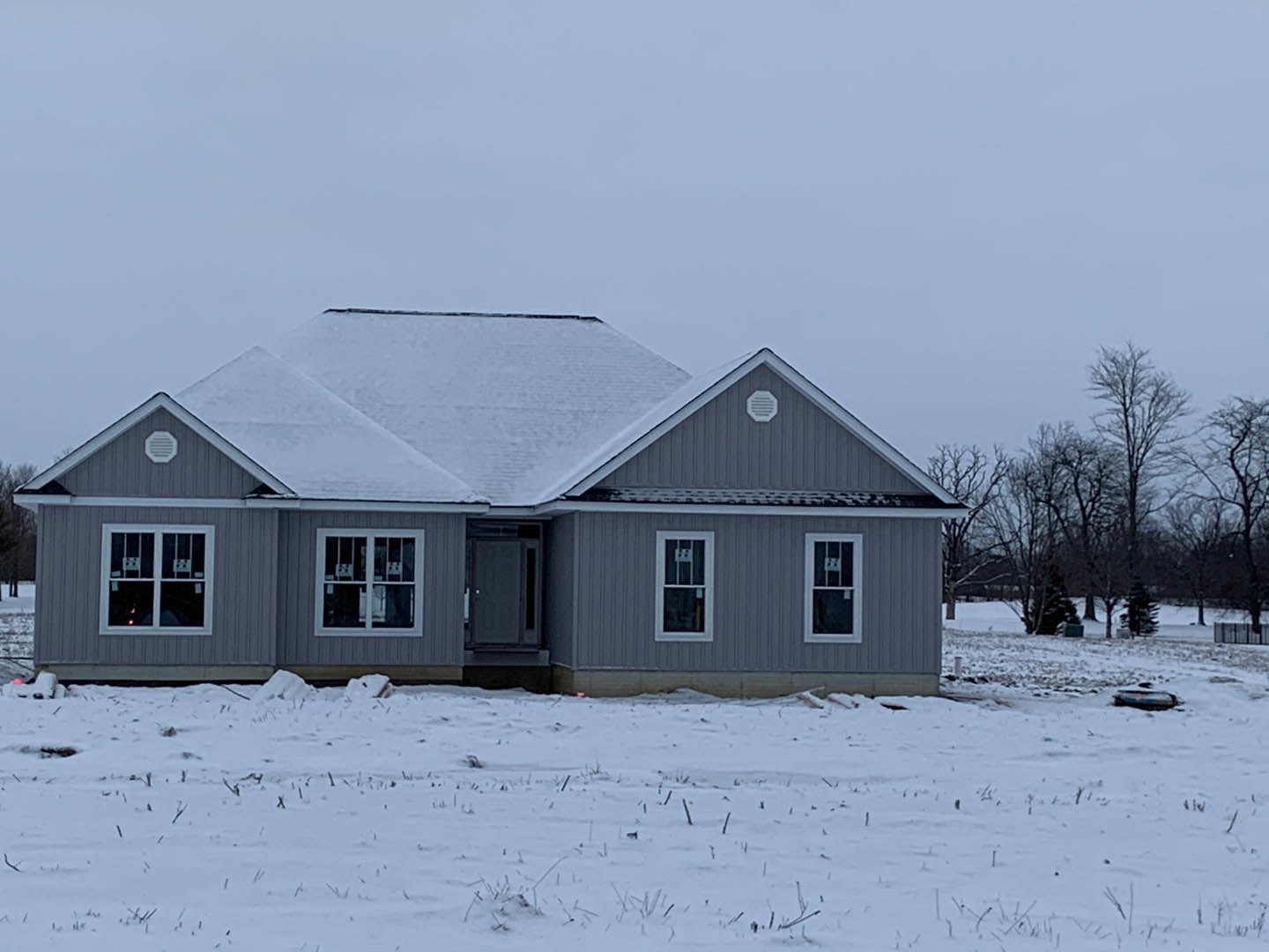 Two-story house with white siding and snow-covered roof, barred window, stickered window, close-up of wooden door, snowy field with scattered sticks in foreground