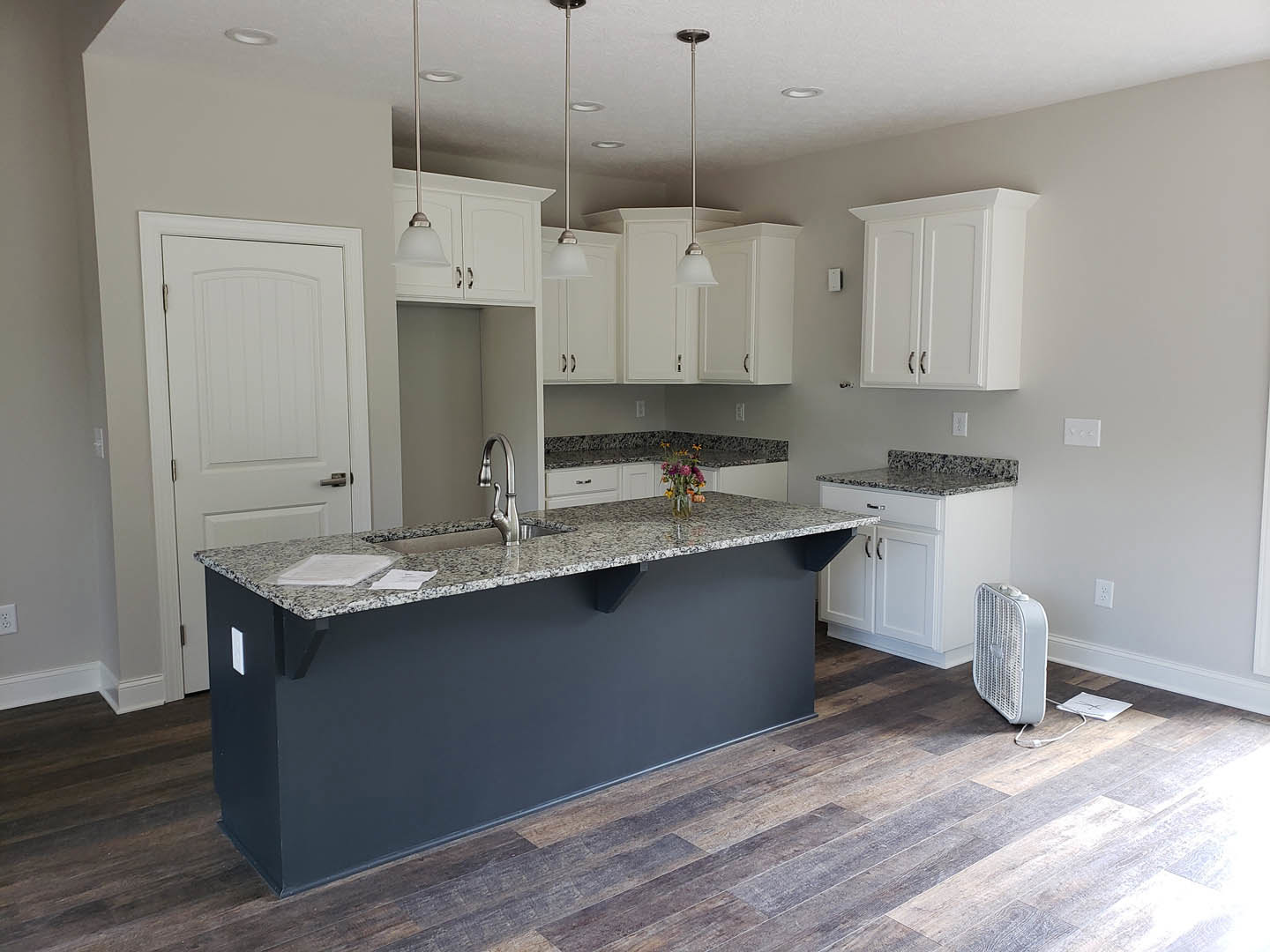 Marble kitchen island with built-in sink and vase of flowers, white cabinetry with black handles, stainless steel appliances, light-colored flooring, and recessed ceiling lighting