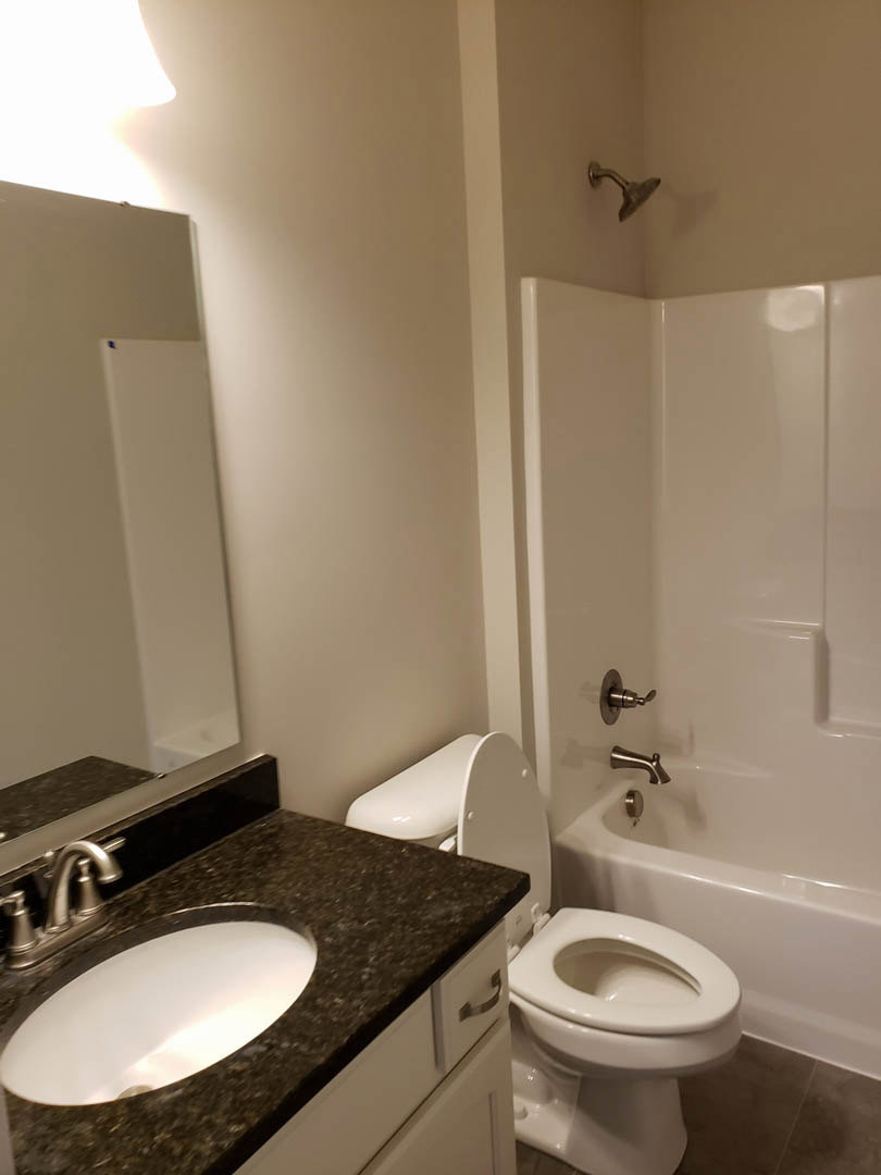 Modern bathroom with white ceramic sink, chrome faucet, glass-enclosed shower, large wall mirror, light gray tile walls, and built-in countertop