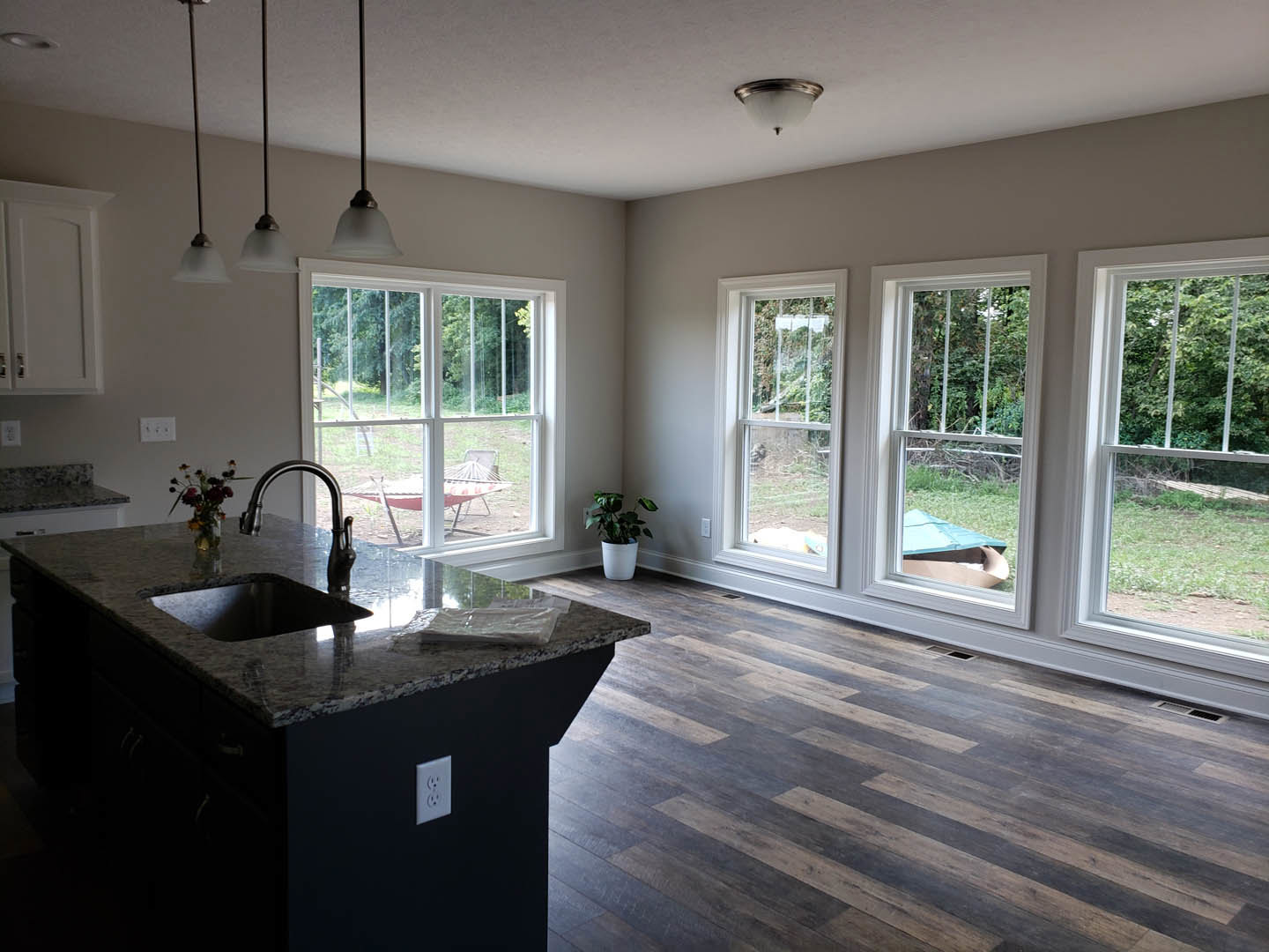 Spacious kitchen featuring a large central island with light countertops, black sink with matching rim, white outlet on the wall, potted plant in the corner, vase of flowers beside