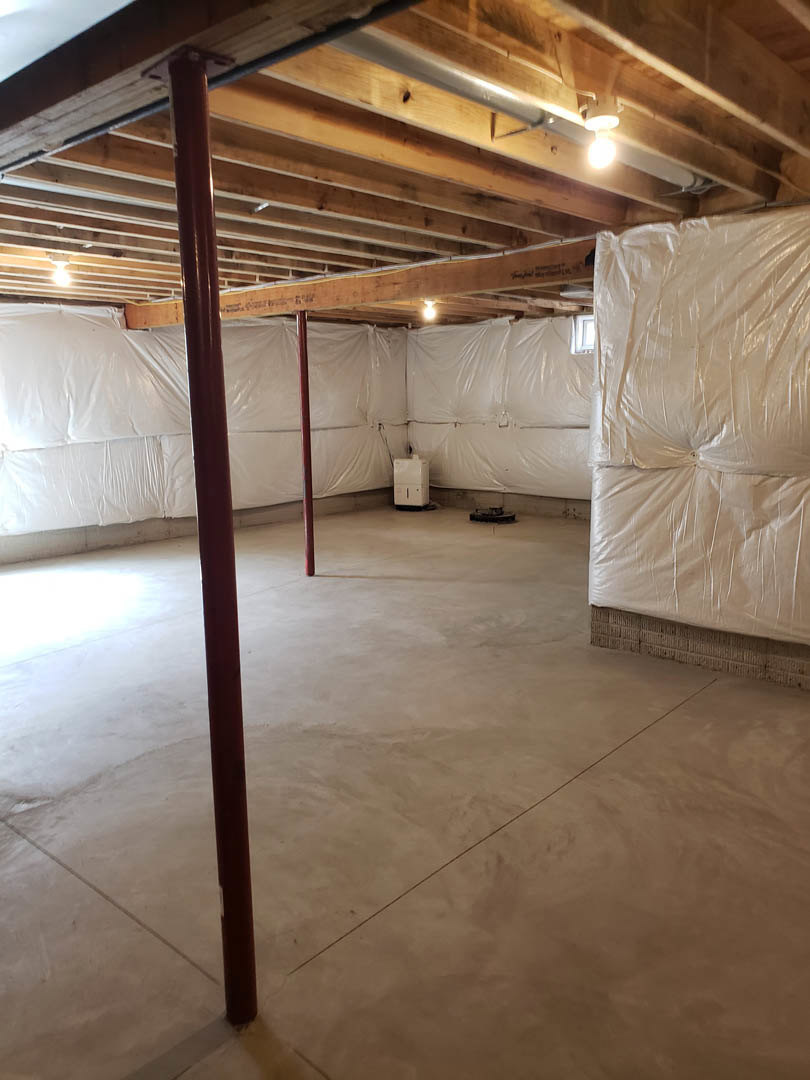 Room under construction with white plastic sheeting covering walls and ceiling, exposed concrete floor, and a red metal support pole.