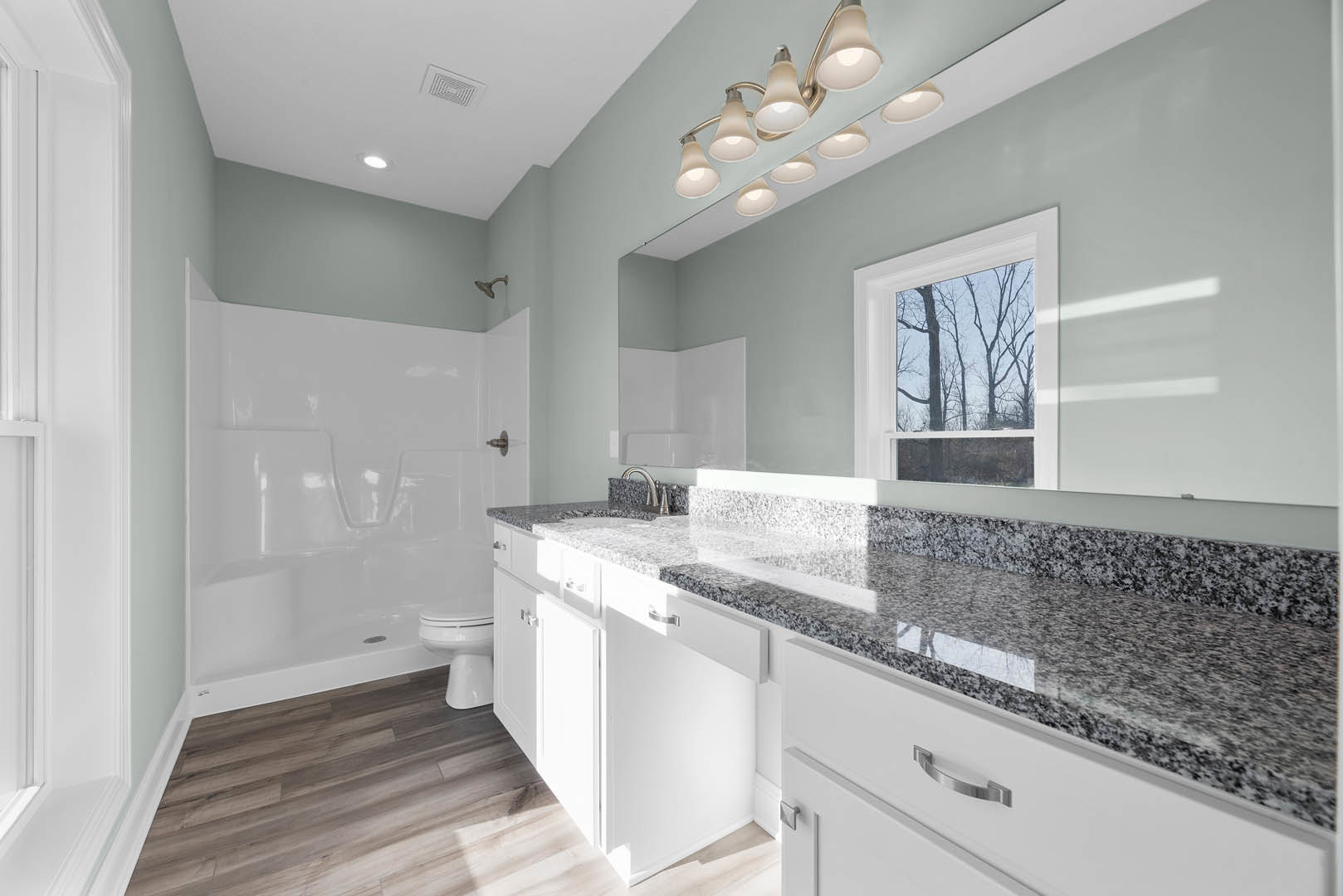 Marble bathroom countertop with white drawers, glass-enclosed shower, white walls, ceiling lights, window overlooking trees, and modern plumbing fixtures