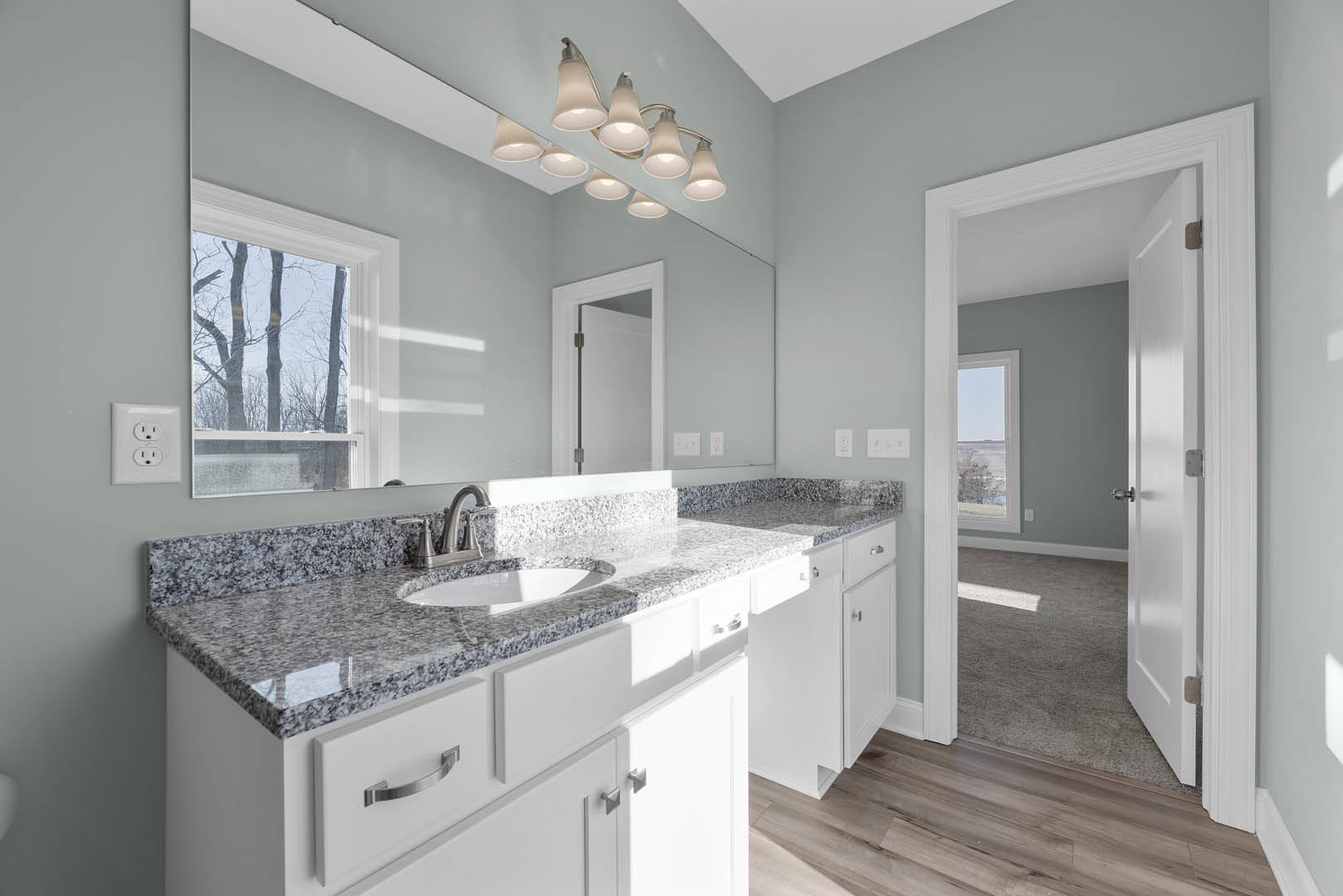 Bathroom featuring a marble countertop with undermount sink, large framed mirror above, white tile walls, chrome faucet, recessed ceiling lights, open door, and window overlooking