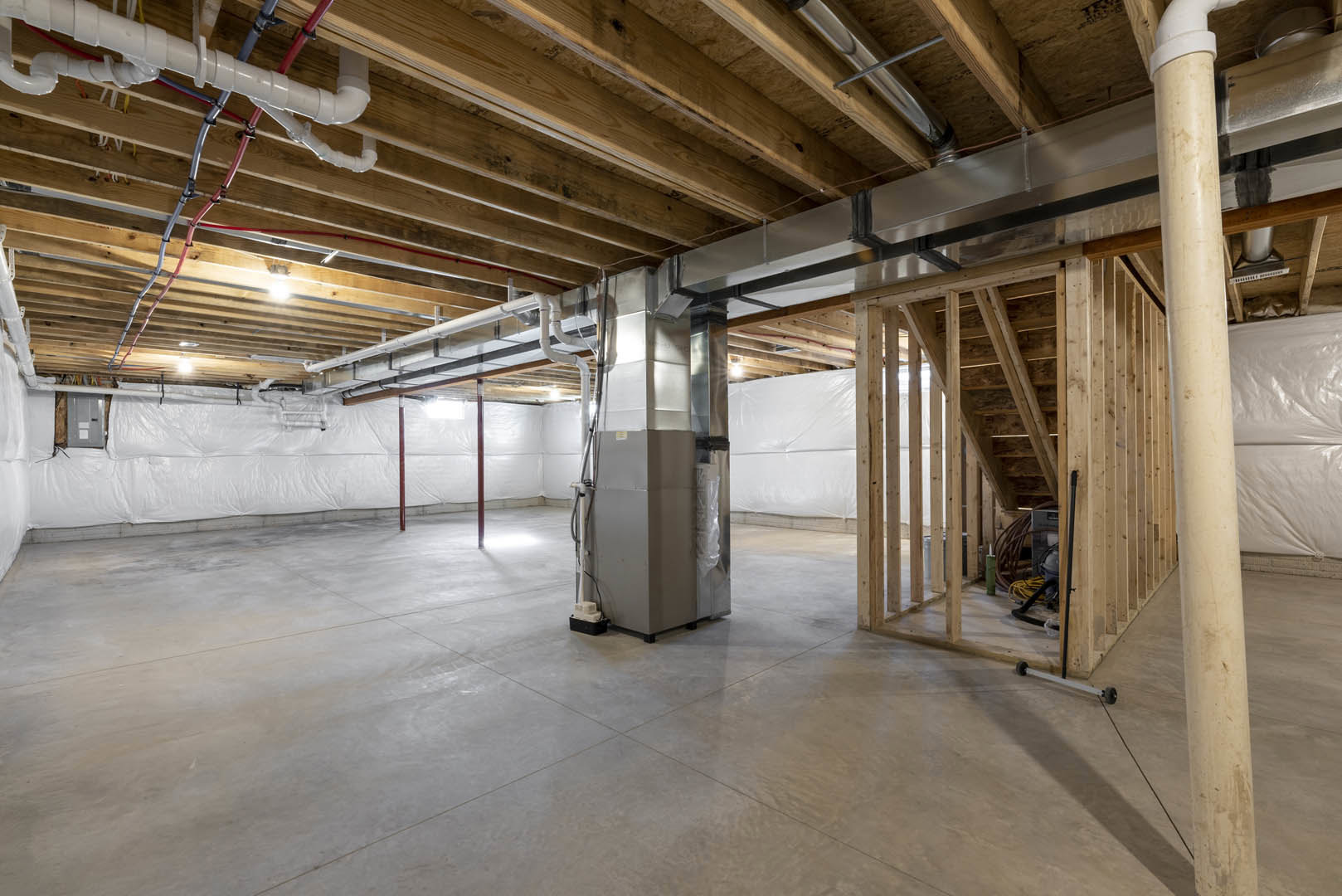 Basement room with exposed wood ceiling beams, steel pipes, metal utility box, and insulated walls
