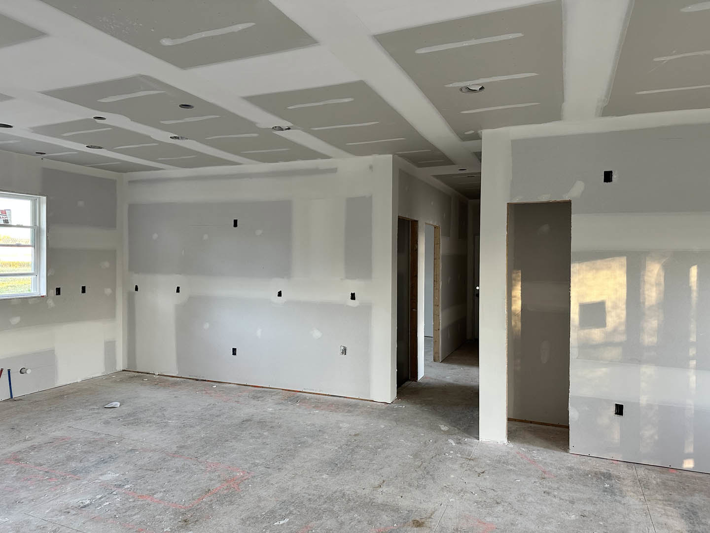 White walls and gray ceiling in a room with concrete flooring, doorway, and window; plaster finishes and composite materials visible.