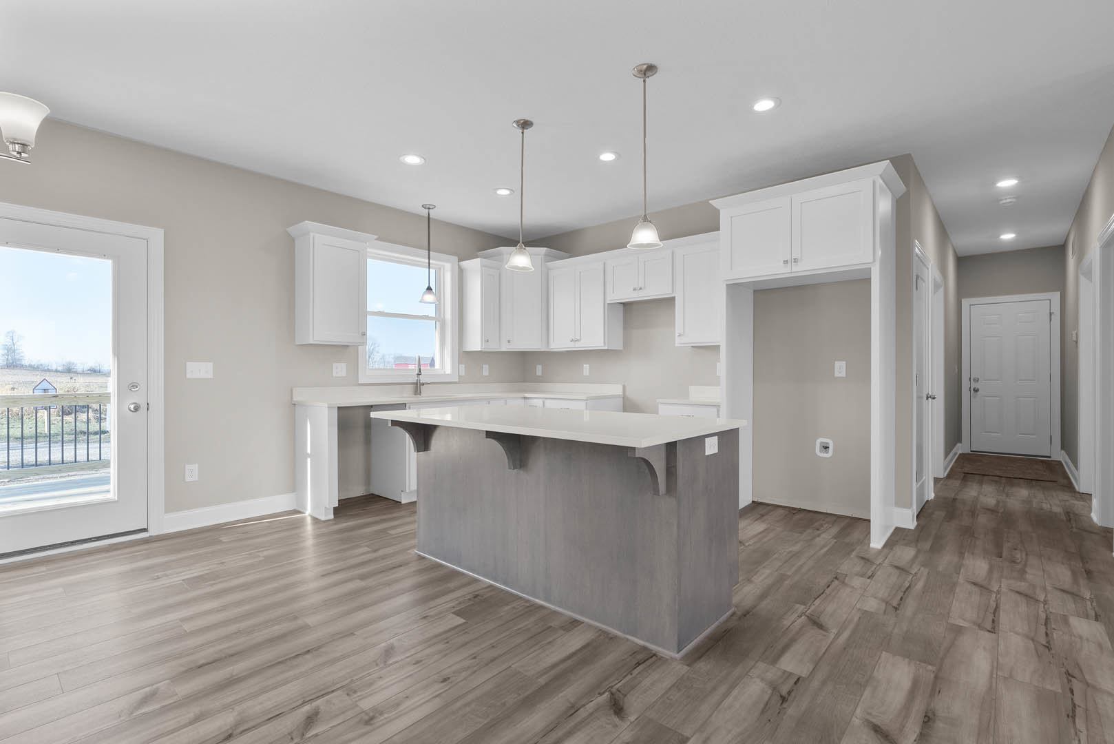 Kitchen with wood flooring, bar-height counter with white cabinetry, stainless steel sink, white walls, open door leading to grassy field, modern ceiling light fixture
