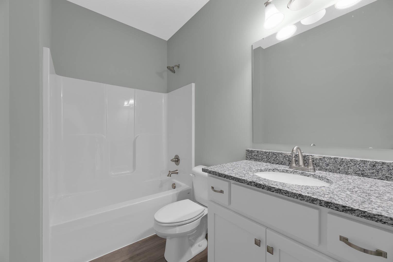 Modern bathroom with white toilet, built-in bathtub, chrome faucet, wall-mounted shower head, light tile walls, and sleek countertop sink