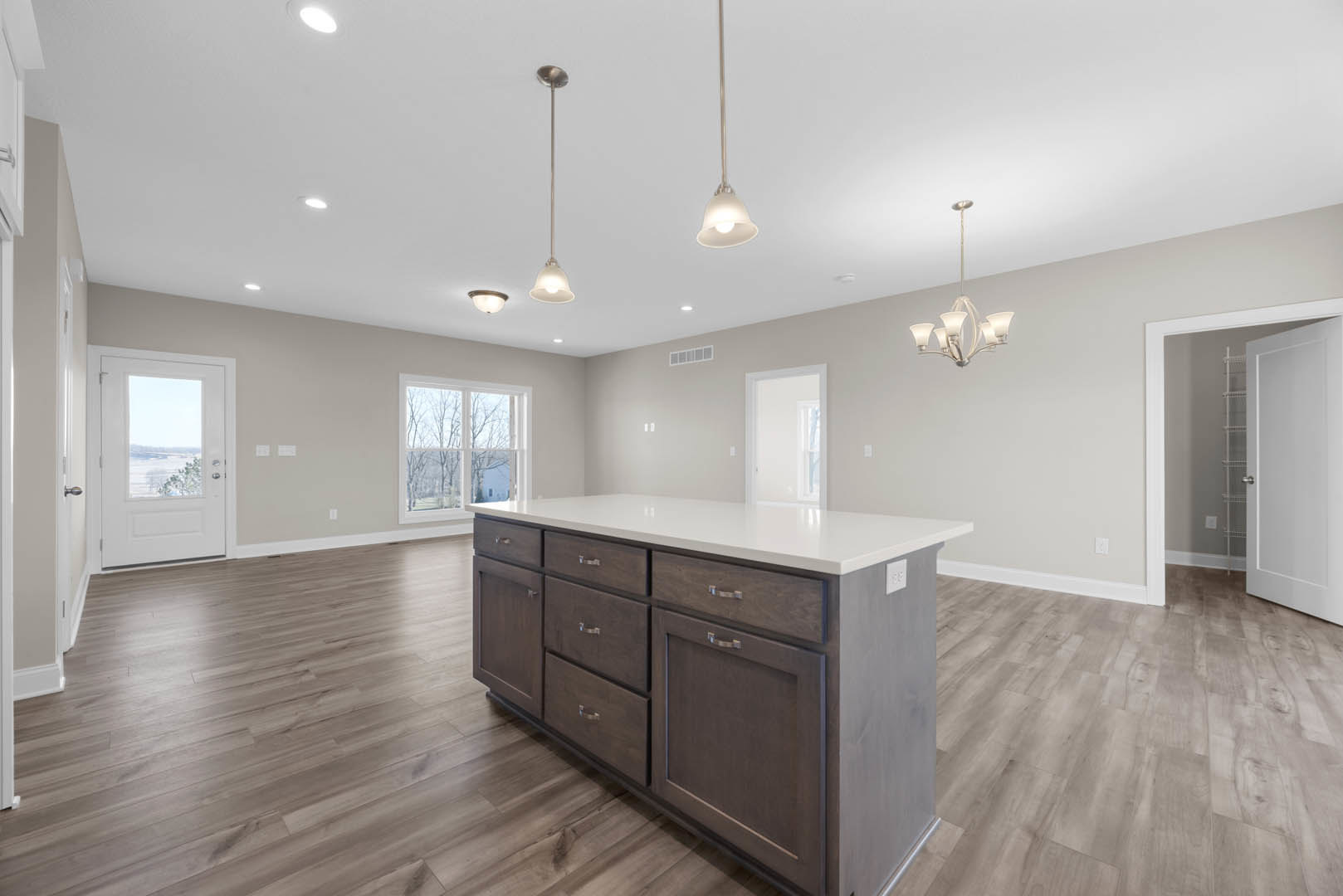 Spacious kitchen featuring a large central island with drawers, white cabinetry, laminate flooring, a chandelier, and a white door with a window overlooking trees