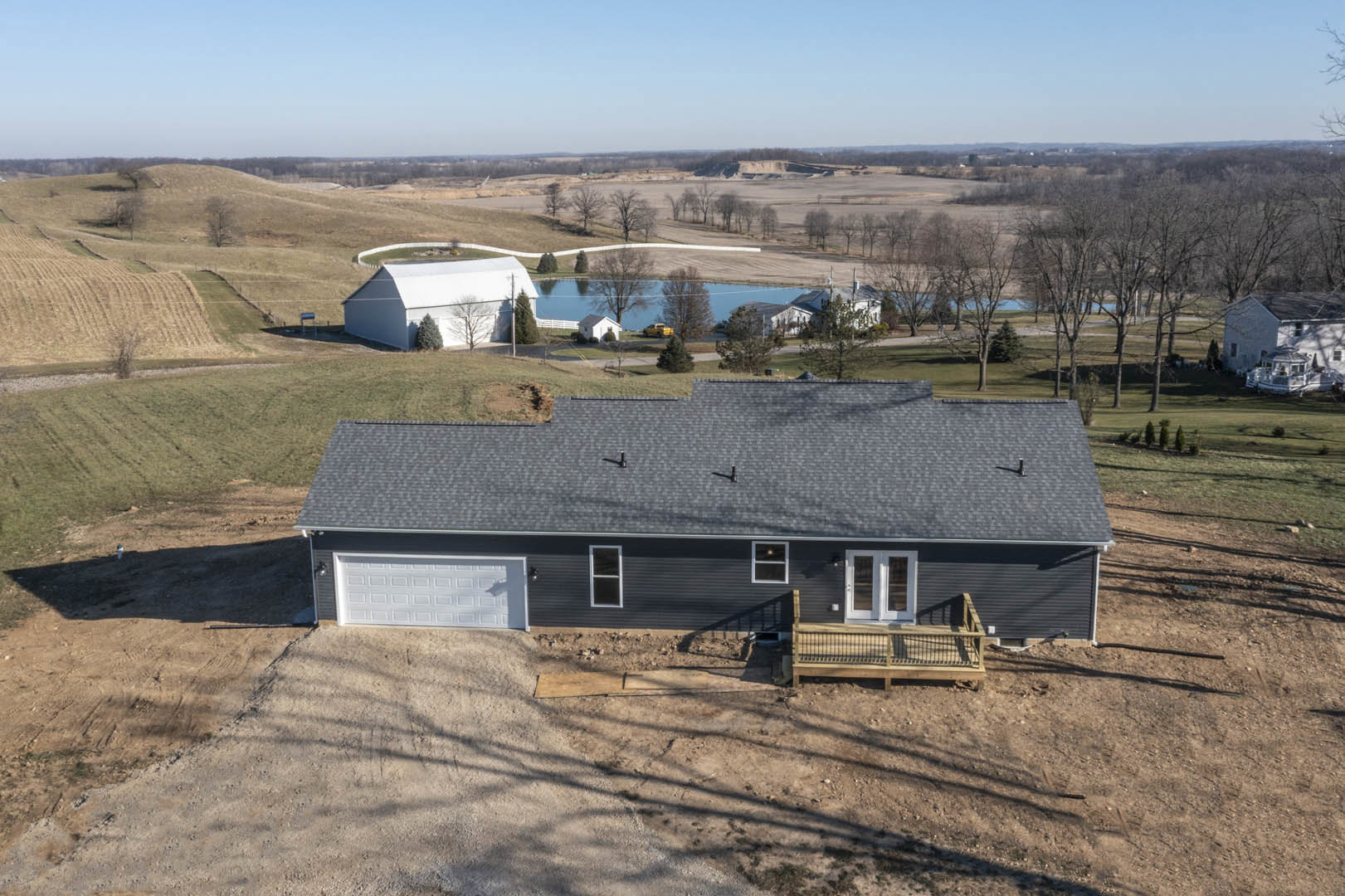 Modern farmhouse with white siding, double glass doors, and attached garage; backyard features a swimming pool, wooden deck with railing, and mature trees.