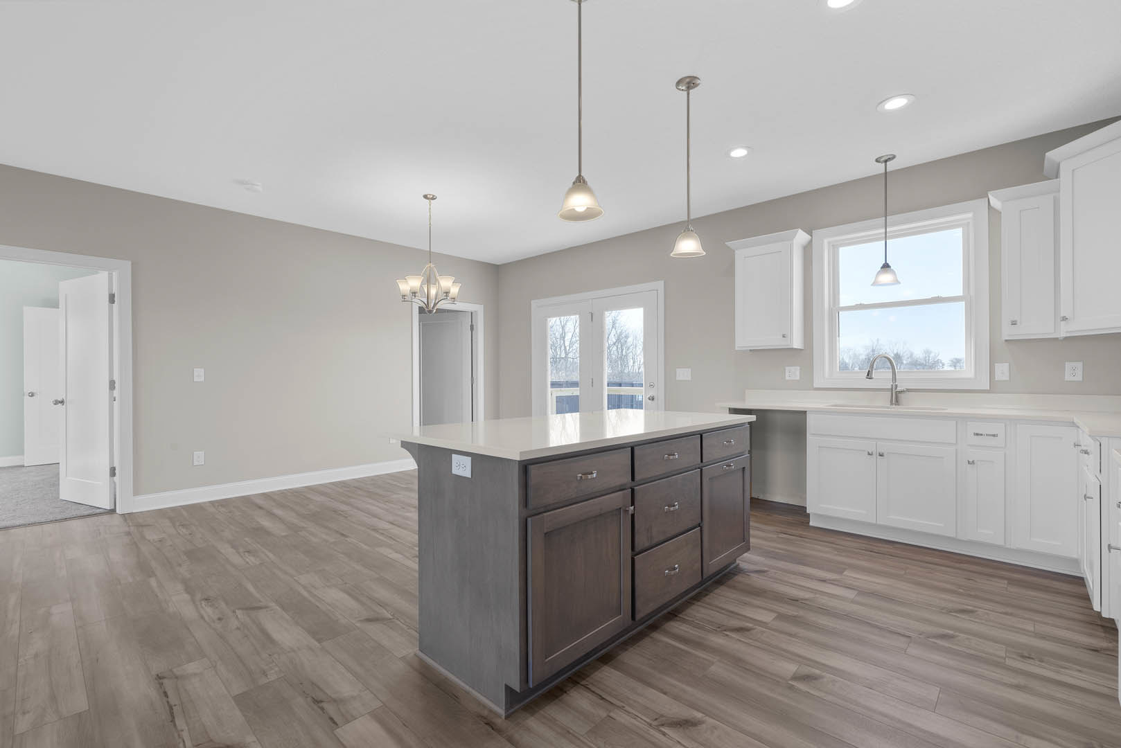 Kitchen with wood flooring, central island featuring drawers, overhead pendant lights, white double doors with glass panes, and stainless steel sink under ceiling lighting