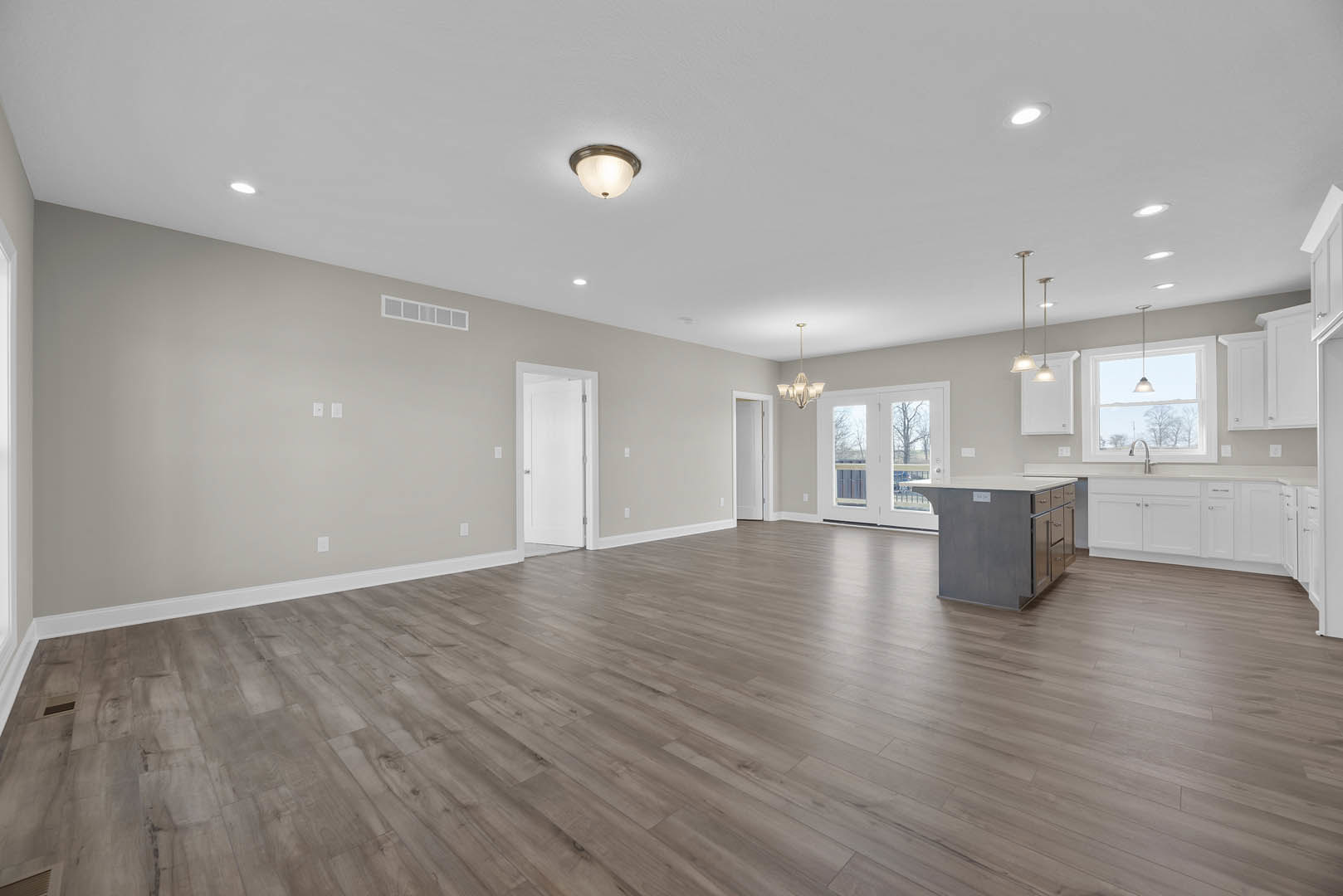 Spacious open-concept interior featuring hardwood floors, central kitchen island with drawers, white door with silver handle, ceiling light fixture, and window overlooking a leafy