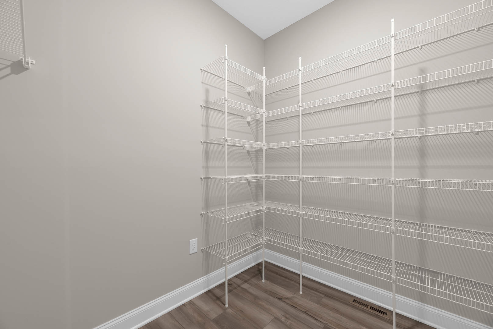 White built-in shelves against a plaster wall, wood flooring with white trim, wall vent, and white ceiling in a corner room.