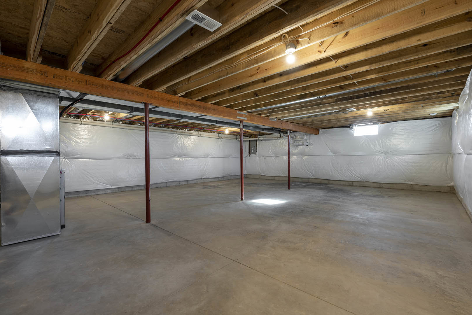 Wooden ceiling with exposed beams, white wall, concrete floor with red support poles, silver triangle with black tape, ceiling-mounted light bulb, white vent attached to a pole