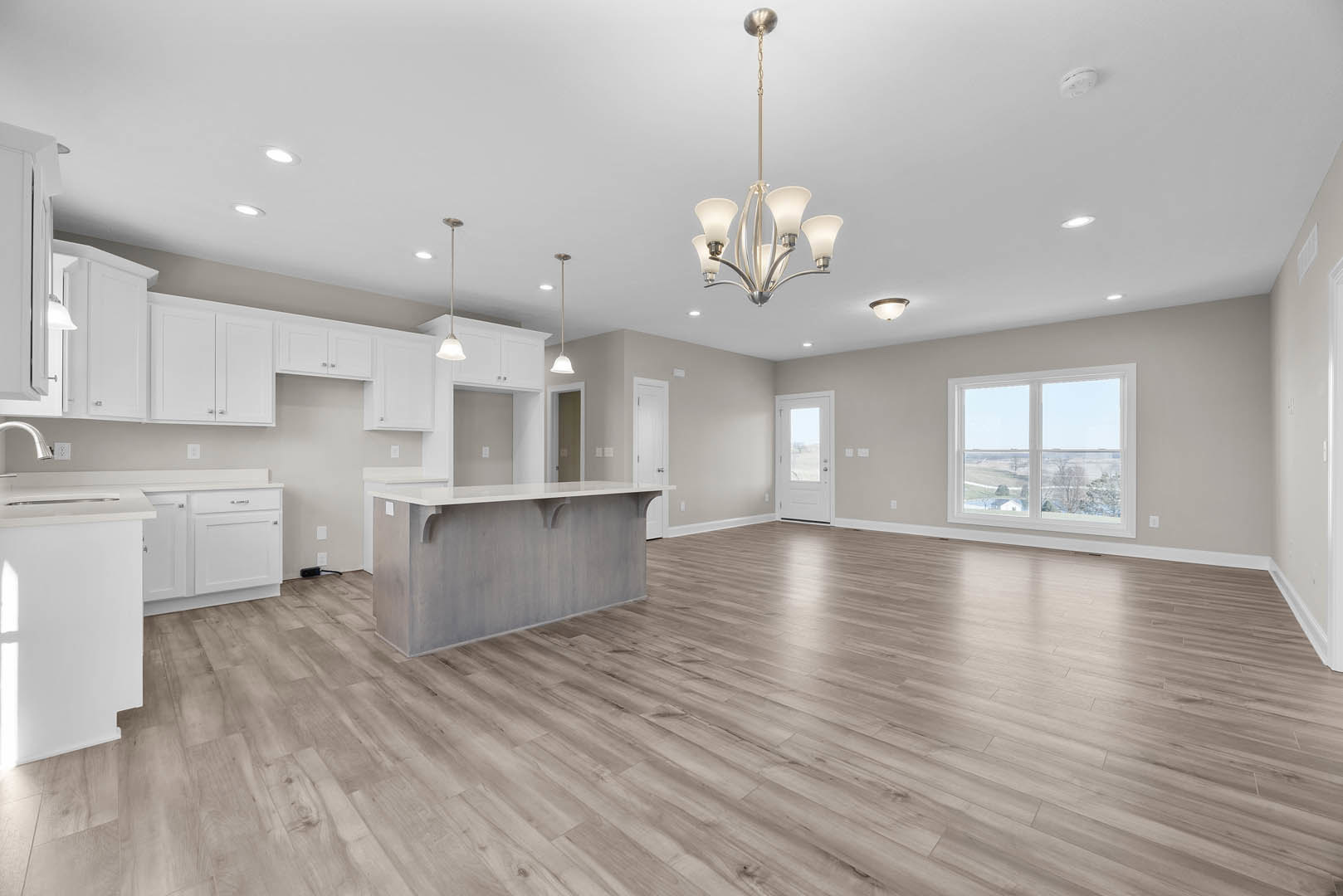 Spacious kitchen with central island, hardwood flooring, white walls, cabinetry, and large window overlooking a field