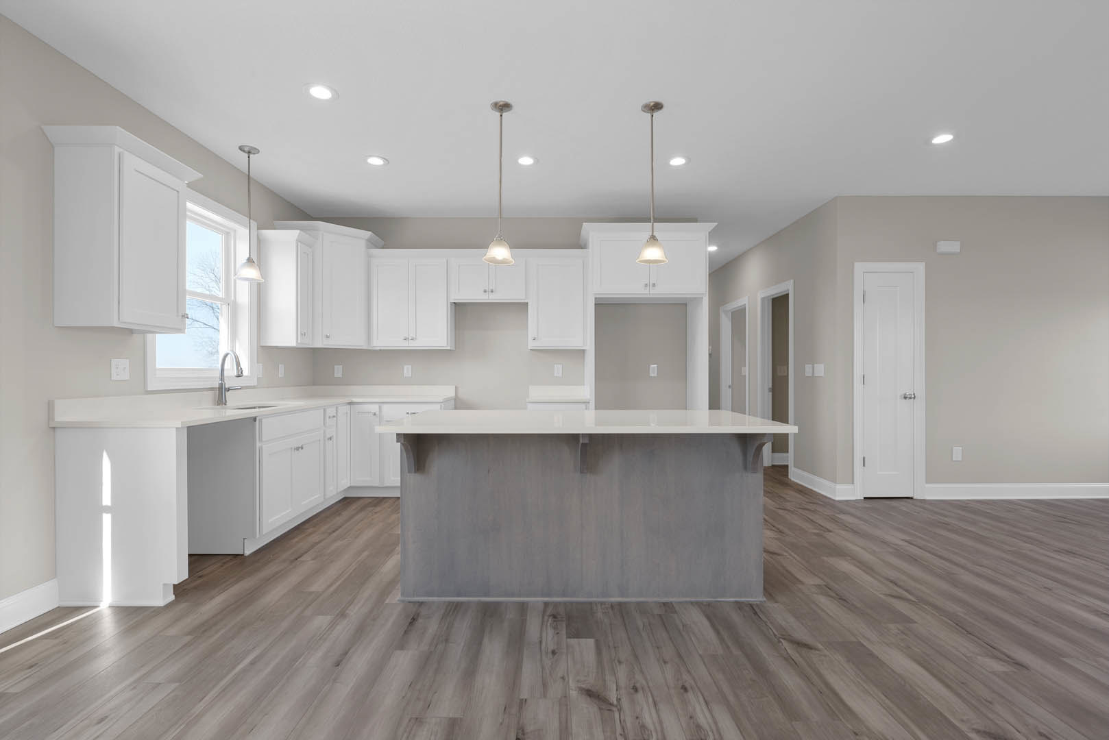 Kitchen featuring white cabinetry, central island with white countertop, wood flooring, ceiling-mounted light fixture, silver door knob on white door, and open shelving along the