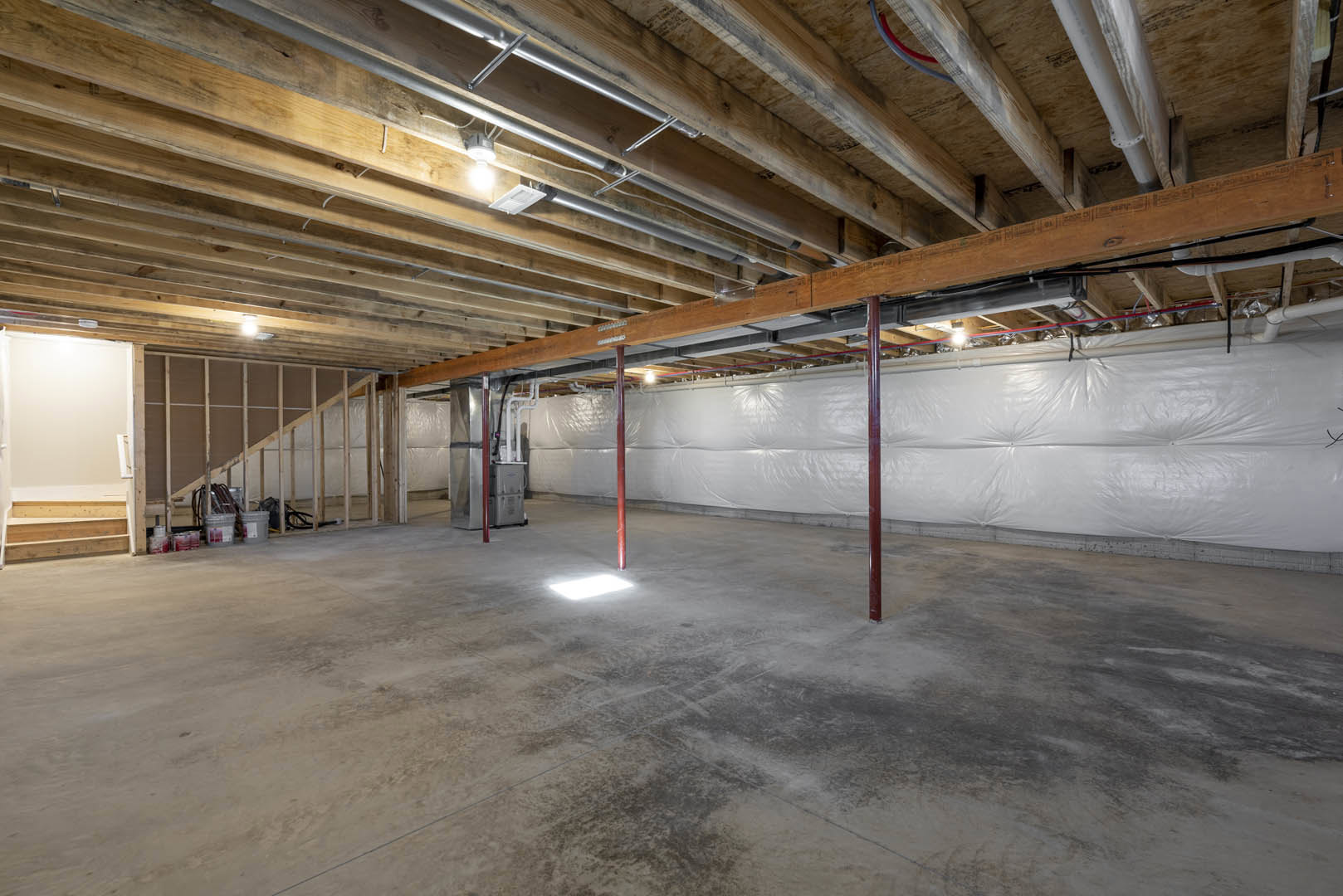 Wood beam ceiling, white walls, concrete floor with red support pole, exposed pipes, unfinished basement interior