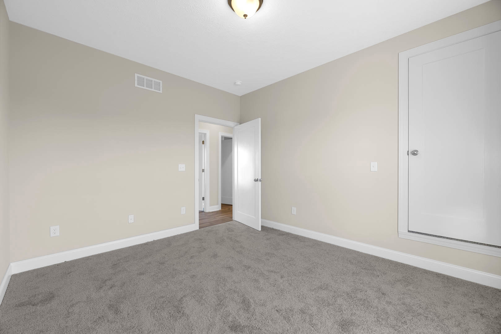 White paneled door with silver handle open to carpeted room, white walls with baseboard molding, ceiling vent visible