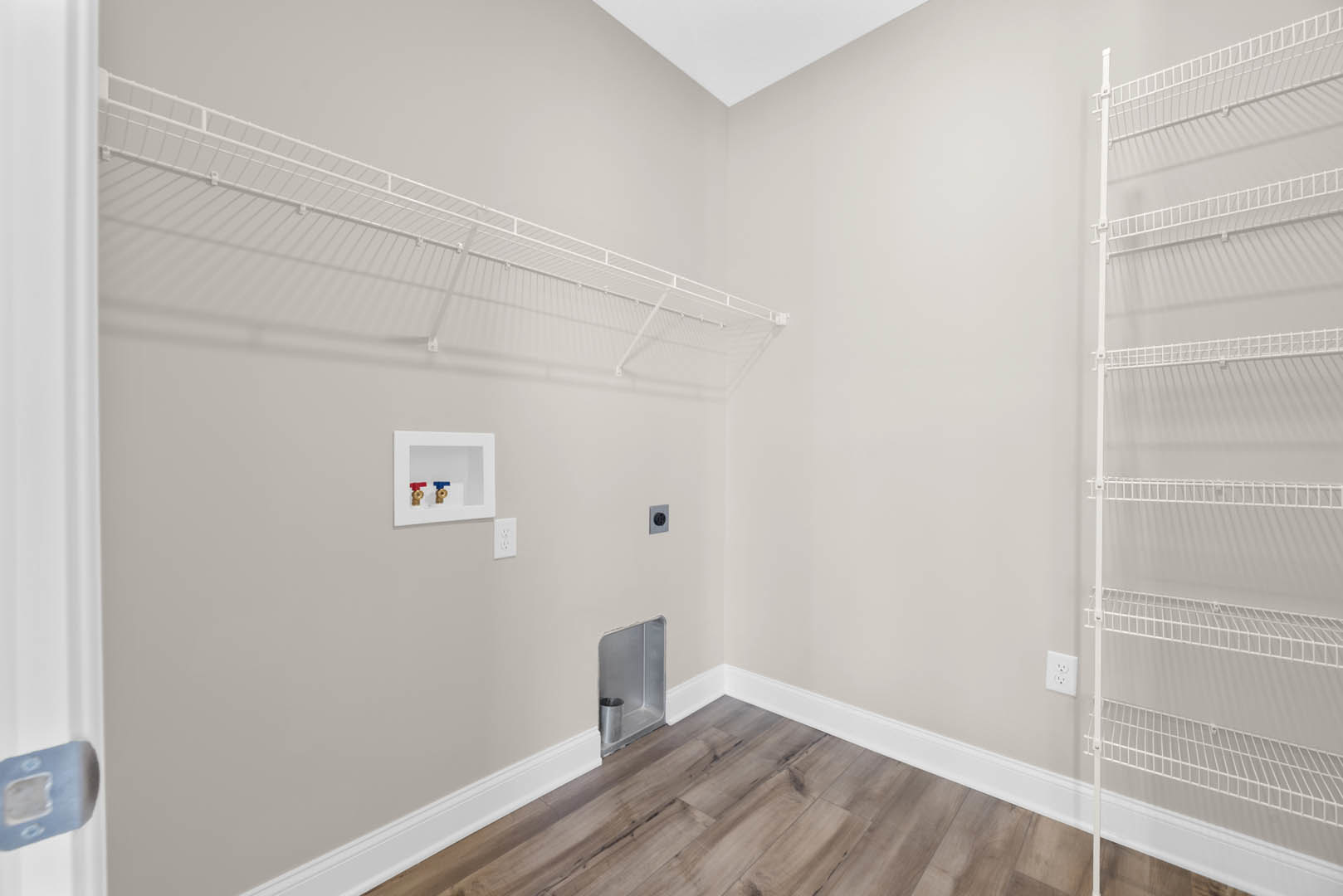 White metal shelf mounted on plaster wall above wood floor with white baseboard, metal cup in corner, square object with two valves visible.