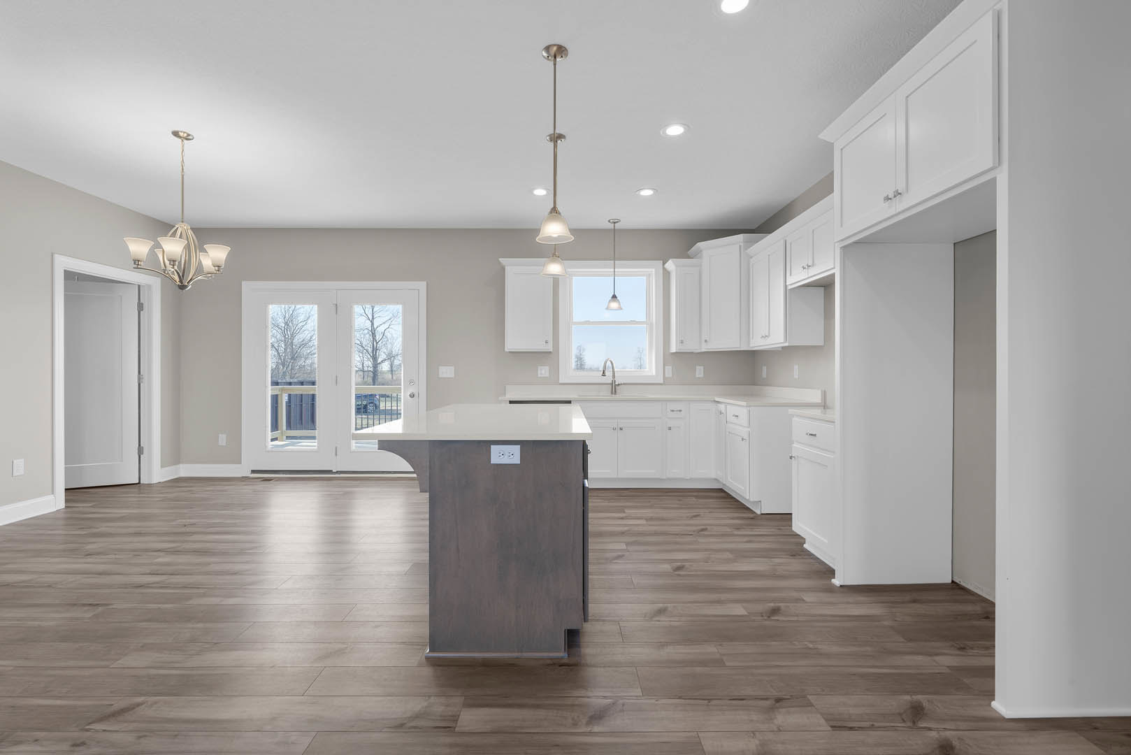 White kitchen cabinets with brushed metal hardware, wood flooring, white double doors with glass panes, white walls, and recessed lighting above a stone countertop.