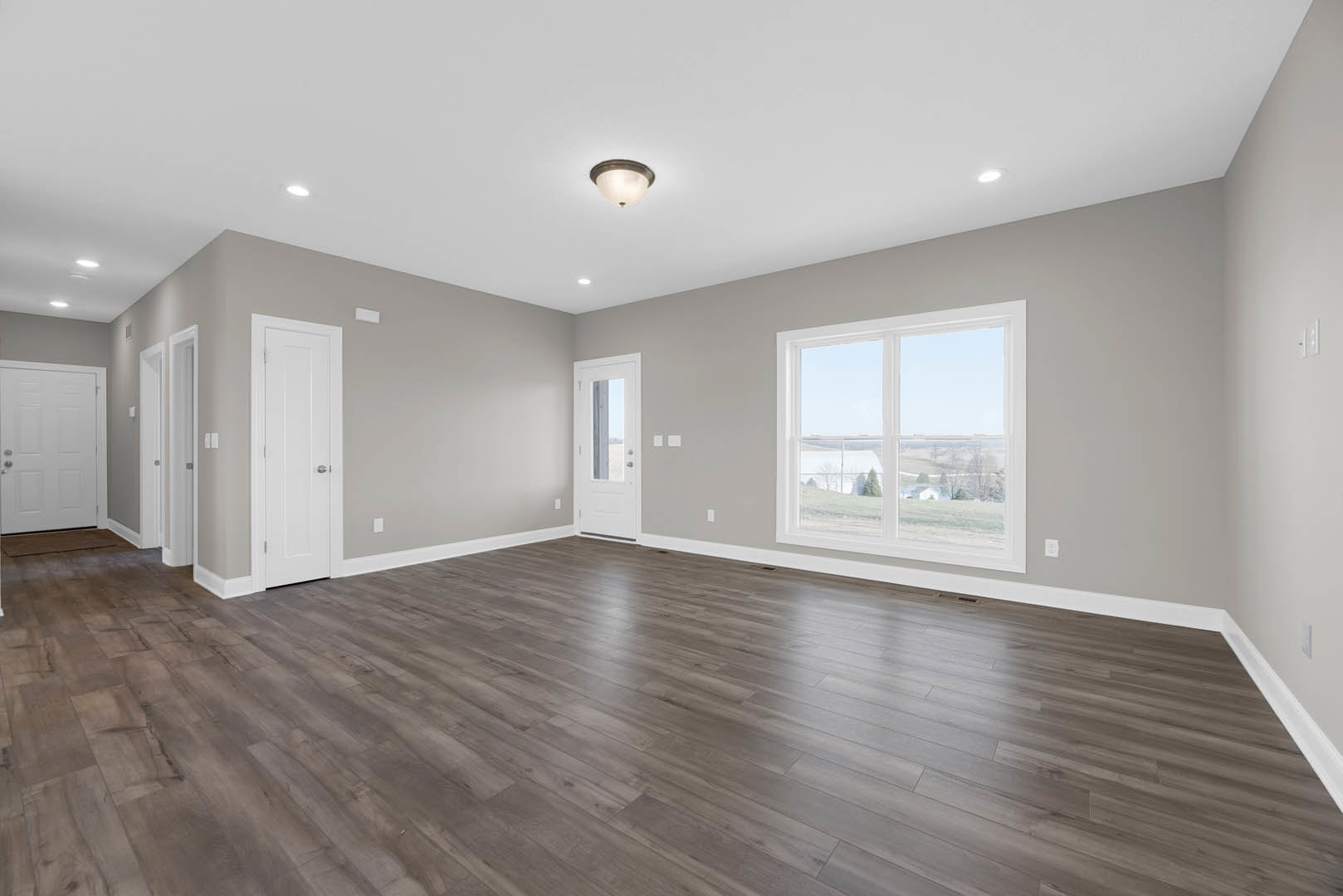 Hardwood floor room with white door featuring silver handle and window, large window overlooking farmland, plaster ceiling and neutral walls