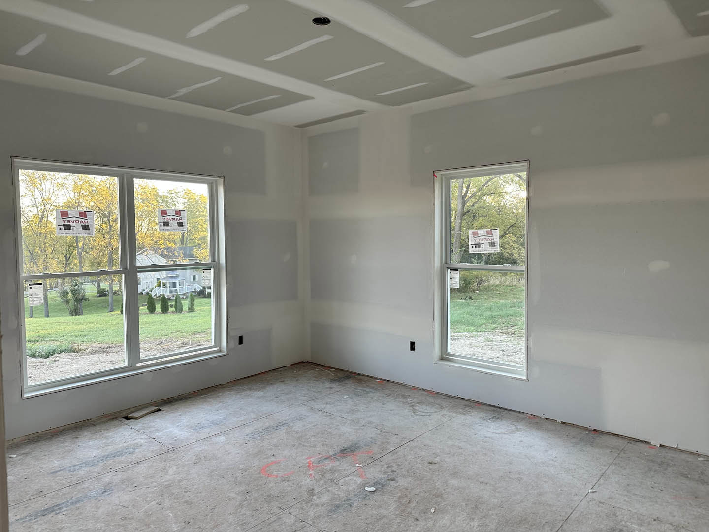 Spacious room with large windows, smooth concrete floor, white plaster walls, and ceiling; red paint accents on floor near window with stickers and sign displaying text.