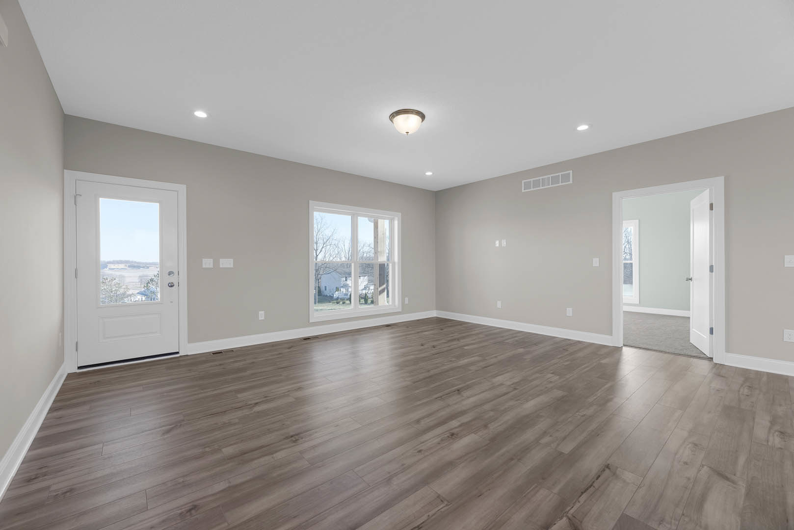 Hardwood floor room with white door featuring glass window, ceiling light fixture, plaster walls, and exterior house visible through window