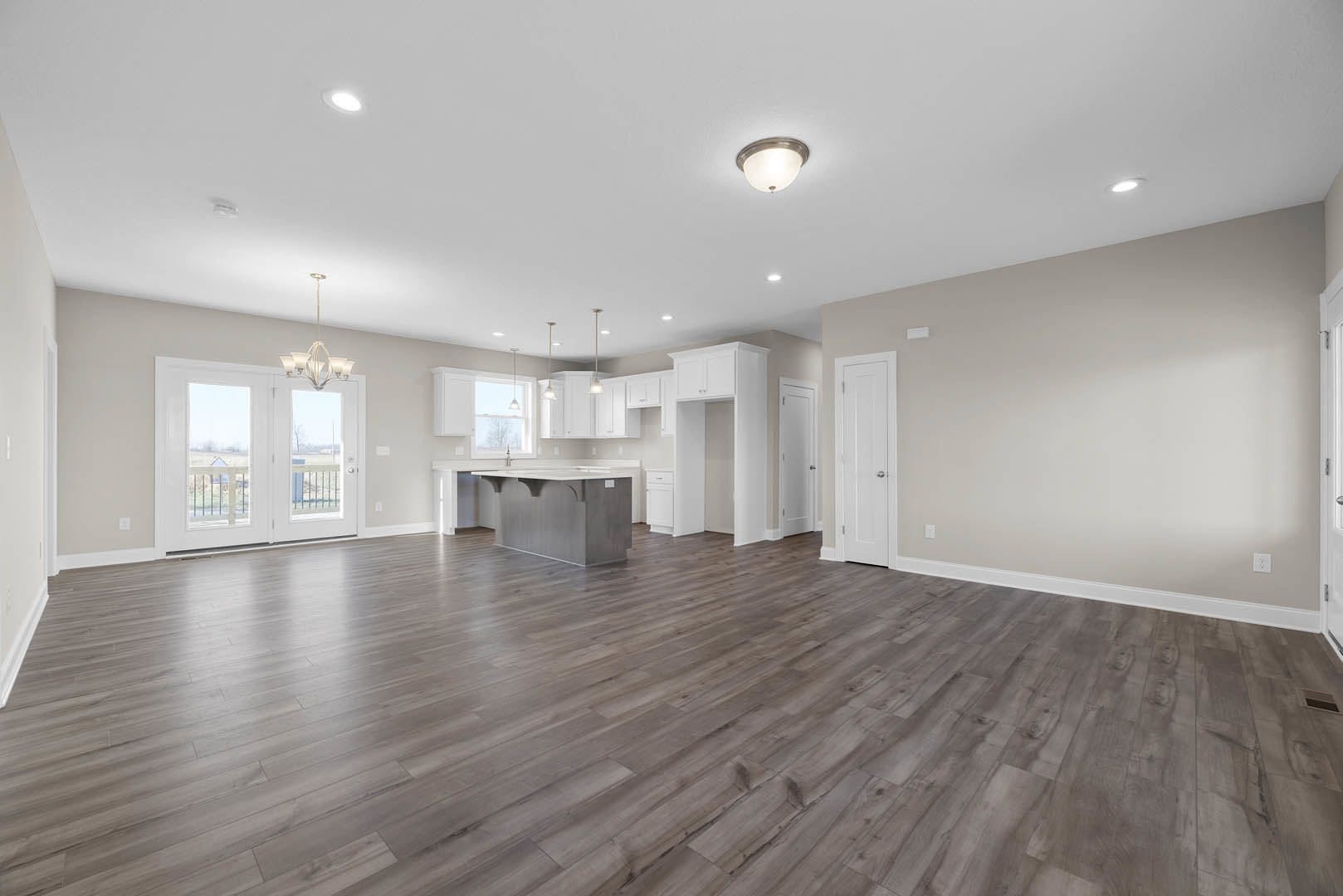 Open-concept kitchen and dining area with wood flooring, white kitchen island, pendant light fixtures, double glass-paneled doors, and white door with silver knobs