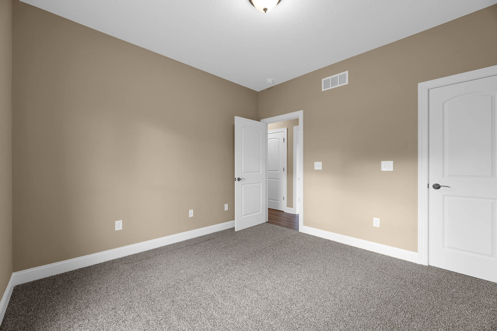 White paneled door with black handle open to carpeted room, white walls, ceiling vent, and simple base molding
