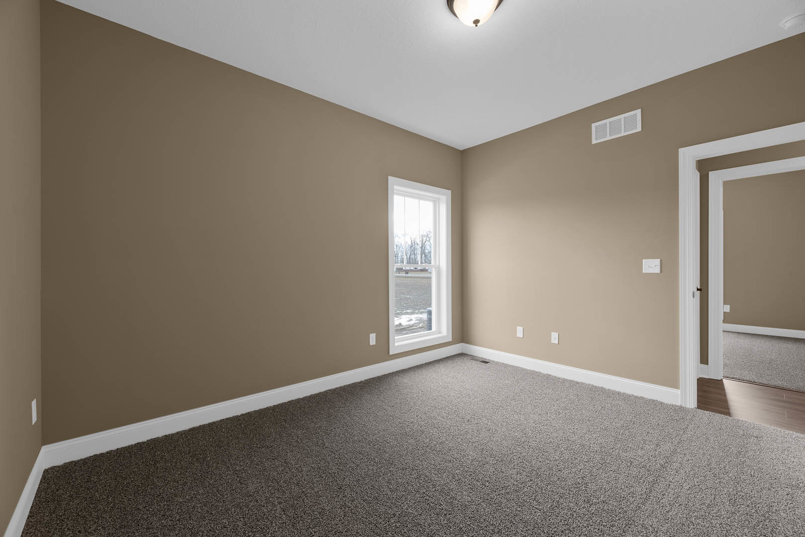 Carpeted bedroom with white walls, large window overlooking field and trees, ceiling vent, recessed light, and crown molding
