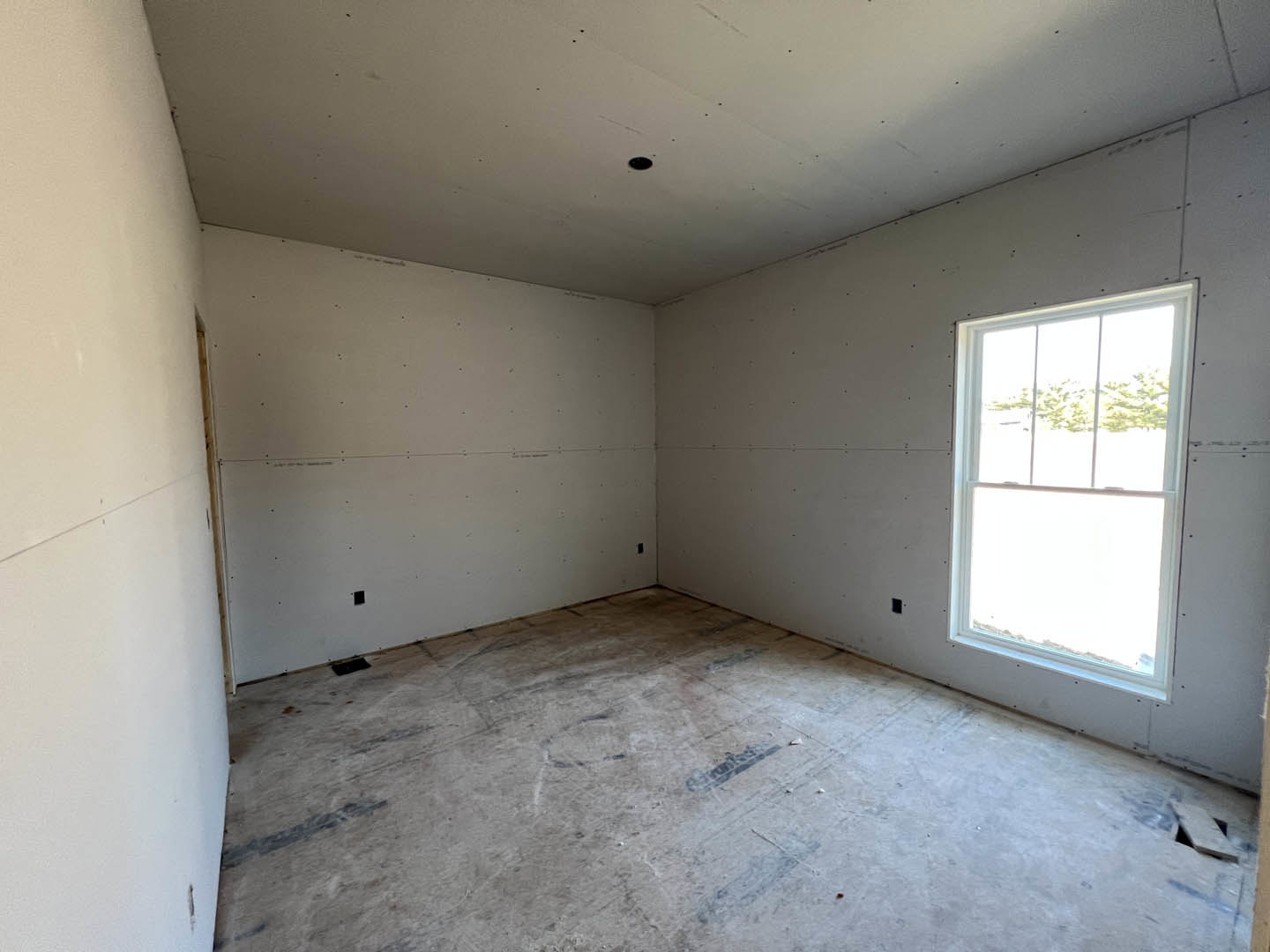 Concrete floor with black marks, white walls, window with white frame, ceiling showing holes, natural daylight entering room
