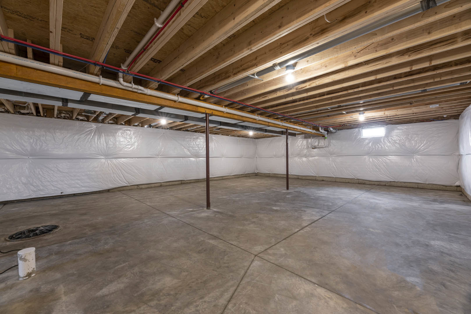White wall with exposed wooden ceiling beams, concrete floor with metal poles, visible ceiling pipes, white cylindrical object with dirt, close-up of tire and light fixture.