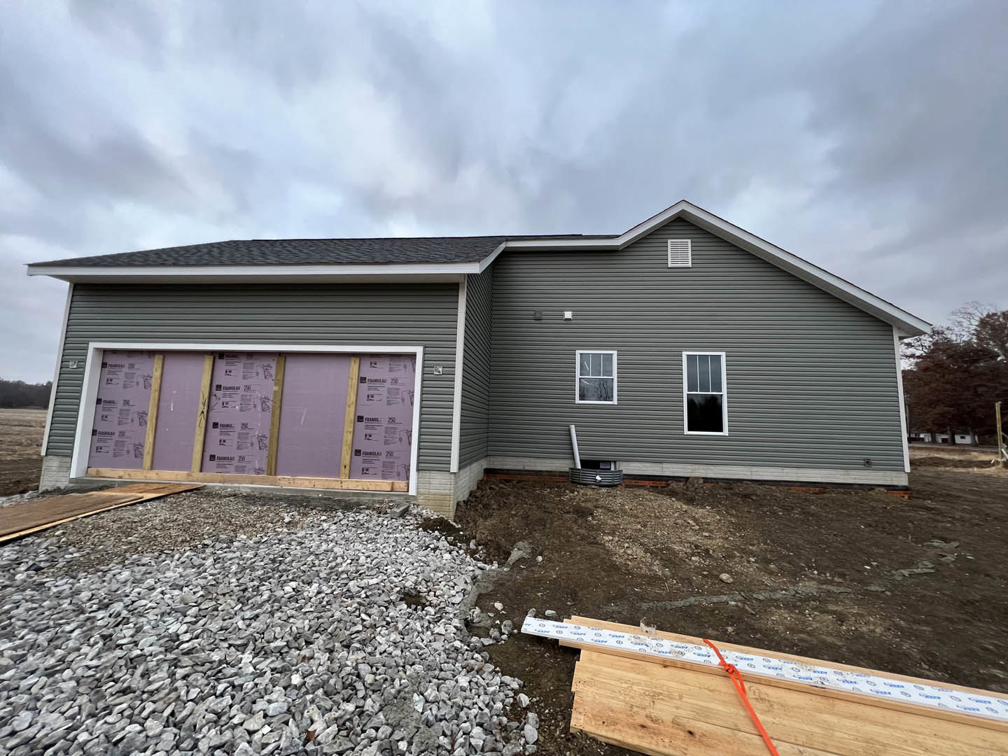 Two-story home with attached garage, light gray siding, white-framed windows, purple front door, and paved driveway under partly cloudy sky.
