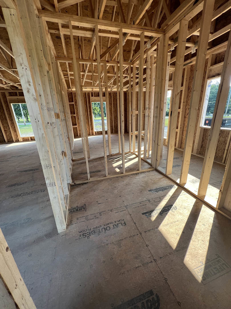 Wood-framed interior room with exposed beams, unfinished concrete floor, and partially installed insulation