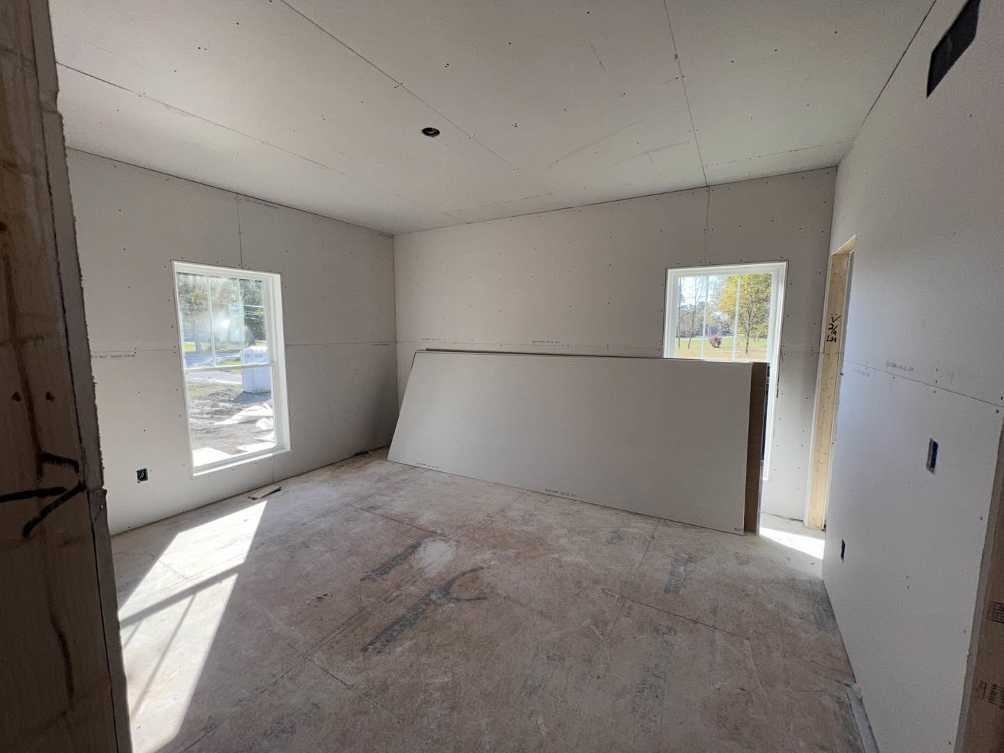 Spacious room featuring a large white plaster wall, expansive windows overlooking trees, concrete flooring, and recessed ceiling detail.